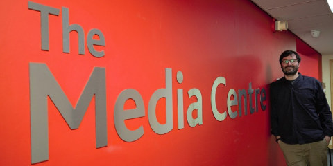 Male stands in front of red wall with The Media Centre in large writing on.