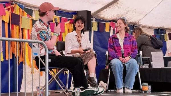 A student sits on stage with two music artists during an interview..