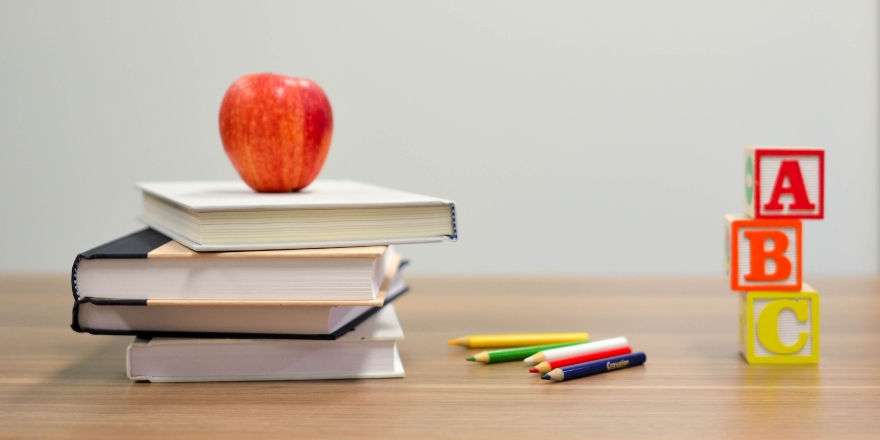 Brown desk with stack of books, red apple and colouring pencils