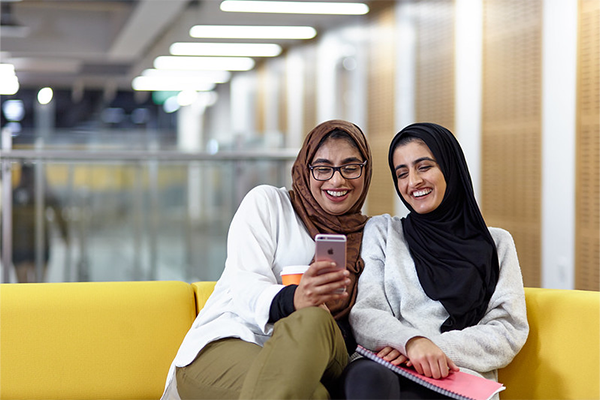 Two students using a phone while sat on a bench.