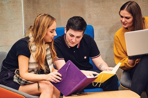 three students helping each other research.