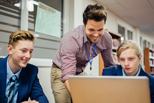 A teacher helping two students at a laptop.