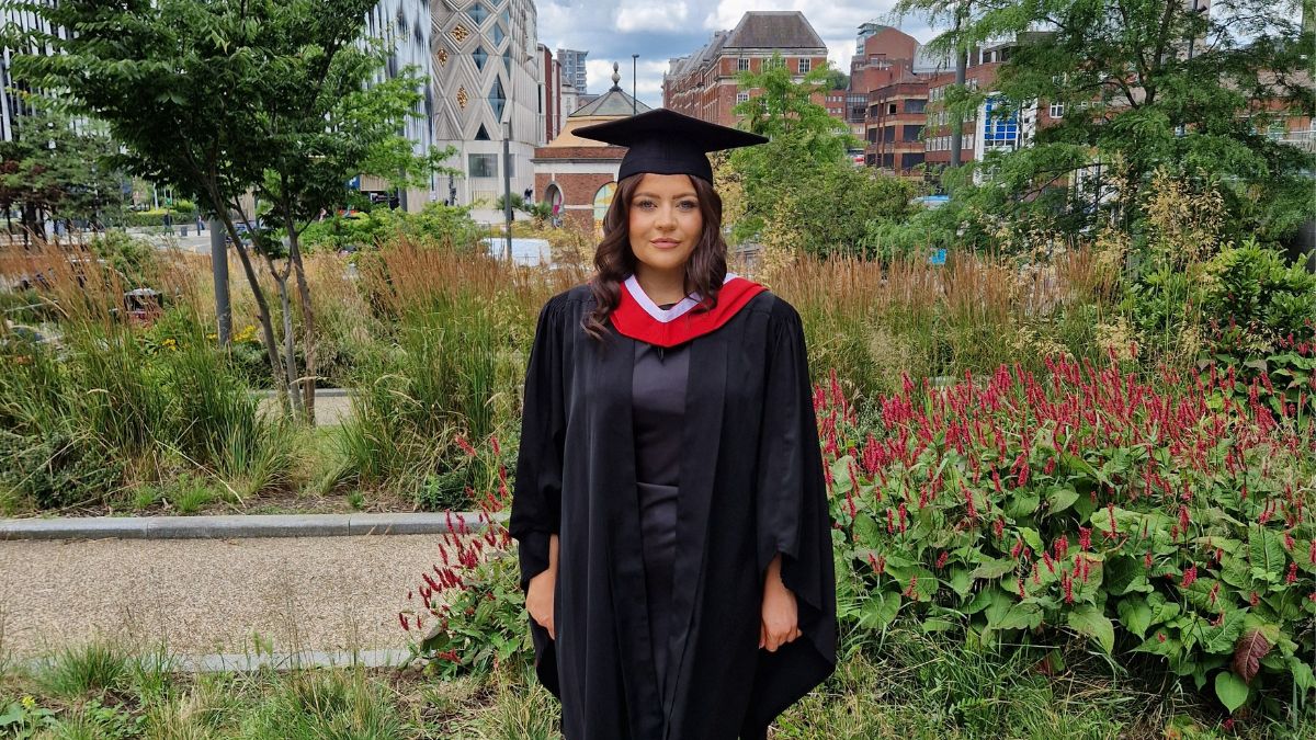 A girl with dark hair wearing a black cap and gown smiles for a picture.