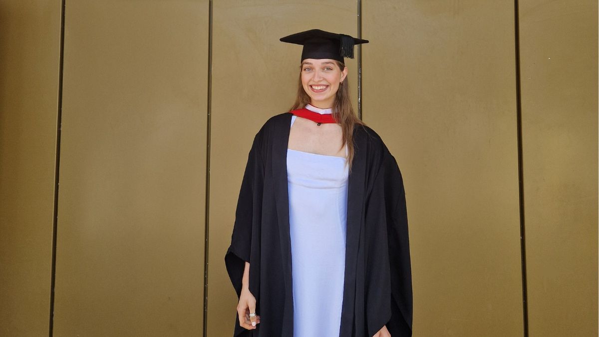 A girl wearing a black cap and gown over a white dress smile for a picture.