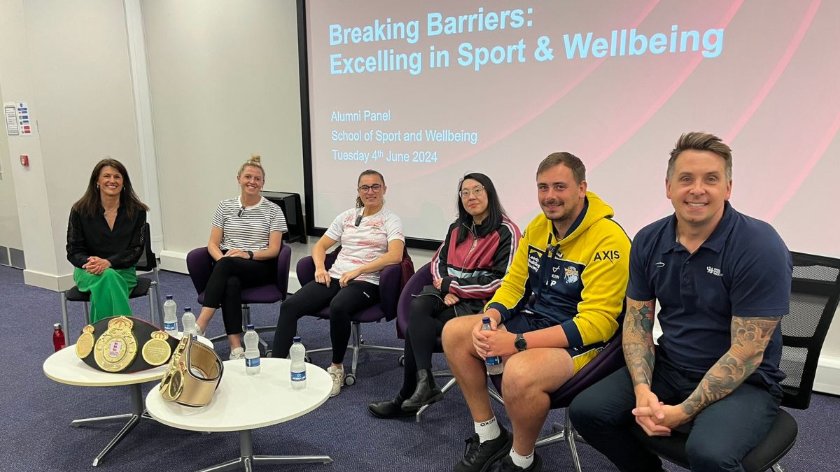 Four women and two men sit in front of a board displaying the words Breaking Barriers.