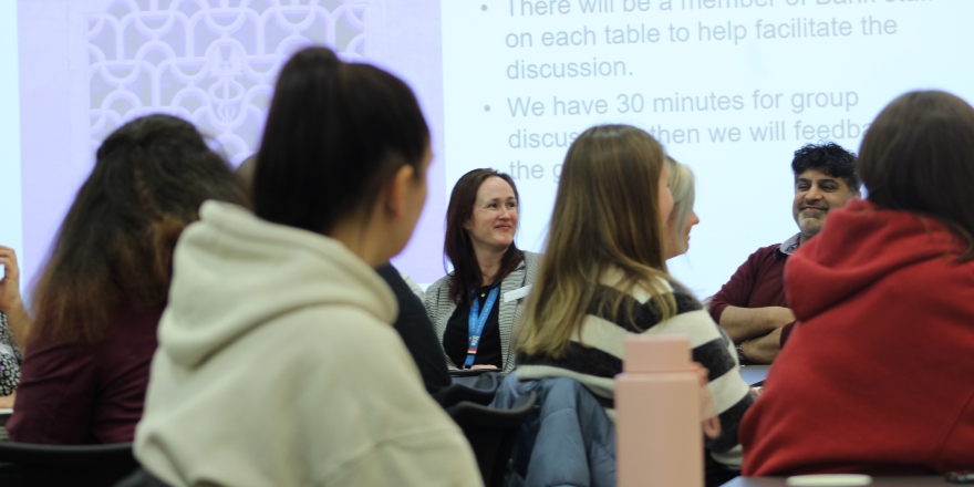 Students facing a screen with a woman and man visible on the panel.