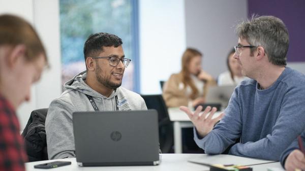 A student sat at a desk listens to an academic.