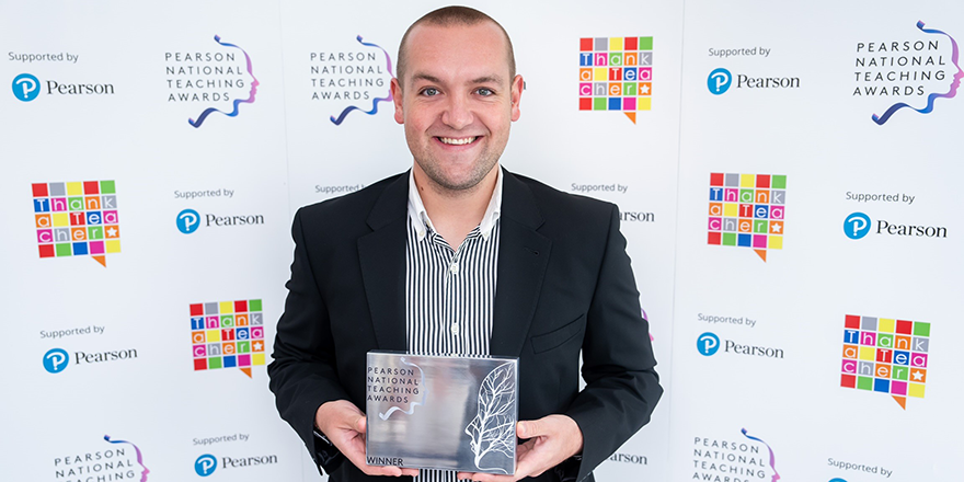 A white man in his 20s smiling and holding a Pearson National Teaching Award..