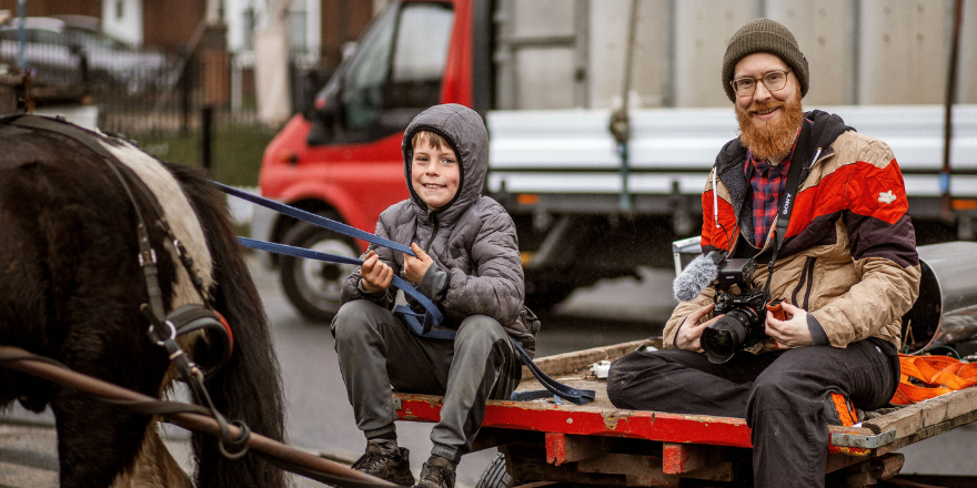 Film maker sat with boy on rag n bone cart.