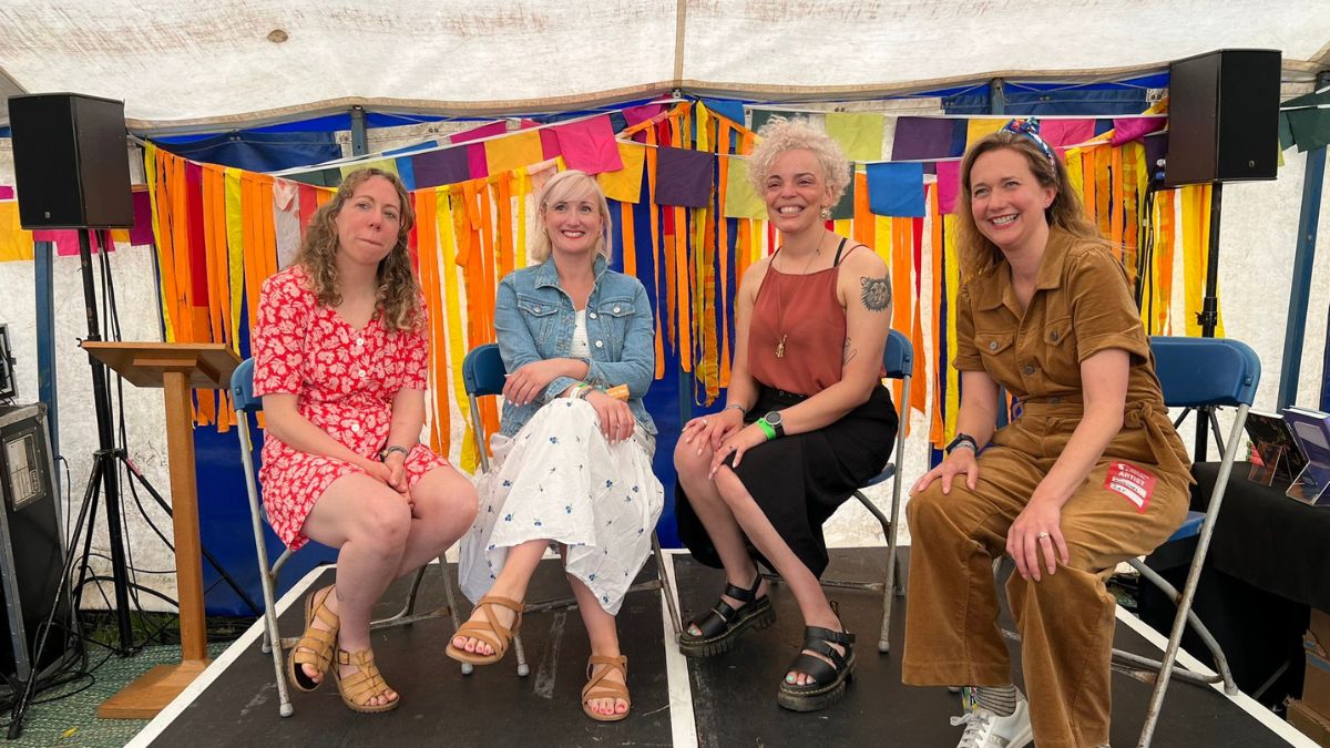 Four women smile while sitting on a stage in front of a colourful background..