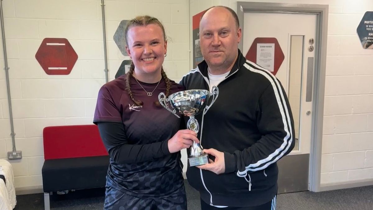 A female student a male member of staff smile while holding a trophy.