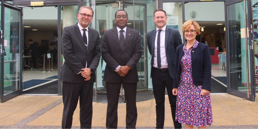 A group of three men and a woman stand outside in front of Leeds Trinity atrium area.