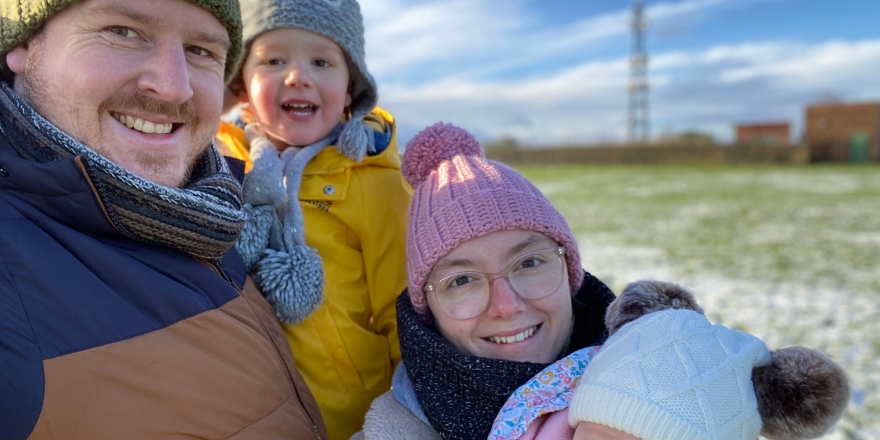 Woman in pink bobble hat, glasses, black scarf with two children and husband.