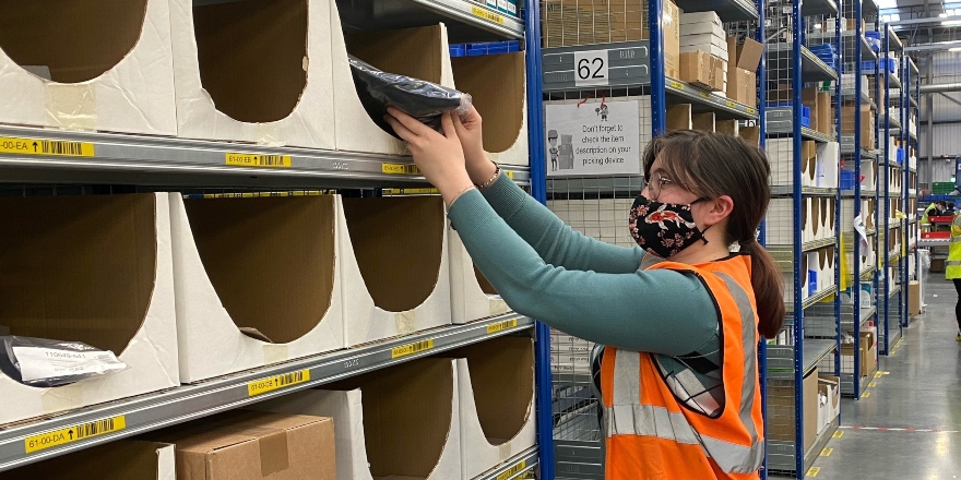 Student stacking shelves in orange hi-vis jacket.