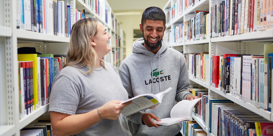 Two students in the library, holding books..