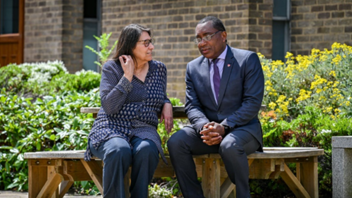 Man and woman both in blue sat on bench talking.