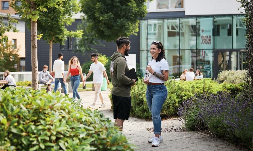 Two students outside on a green campus, in front of the Atrium.