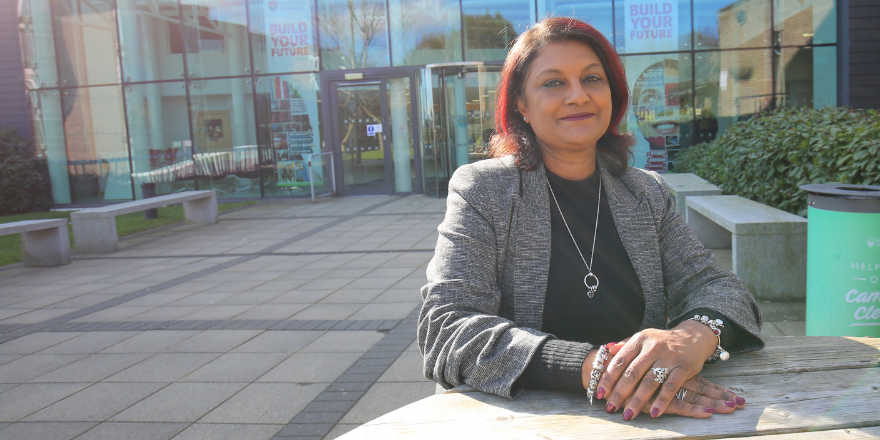 Female lecturer sat on bench in front of university building.