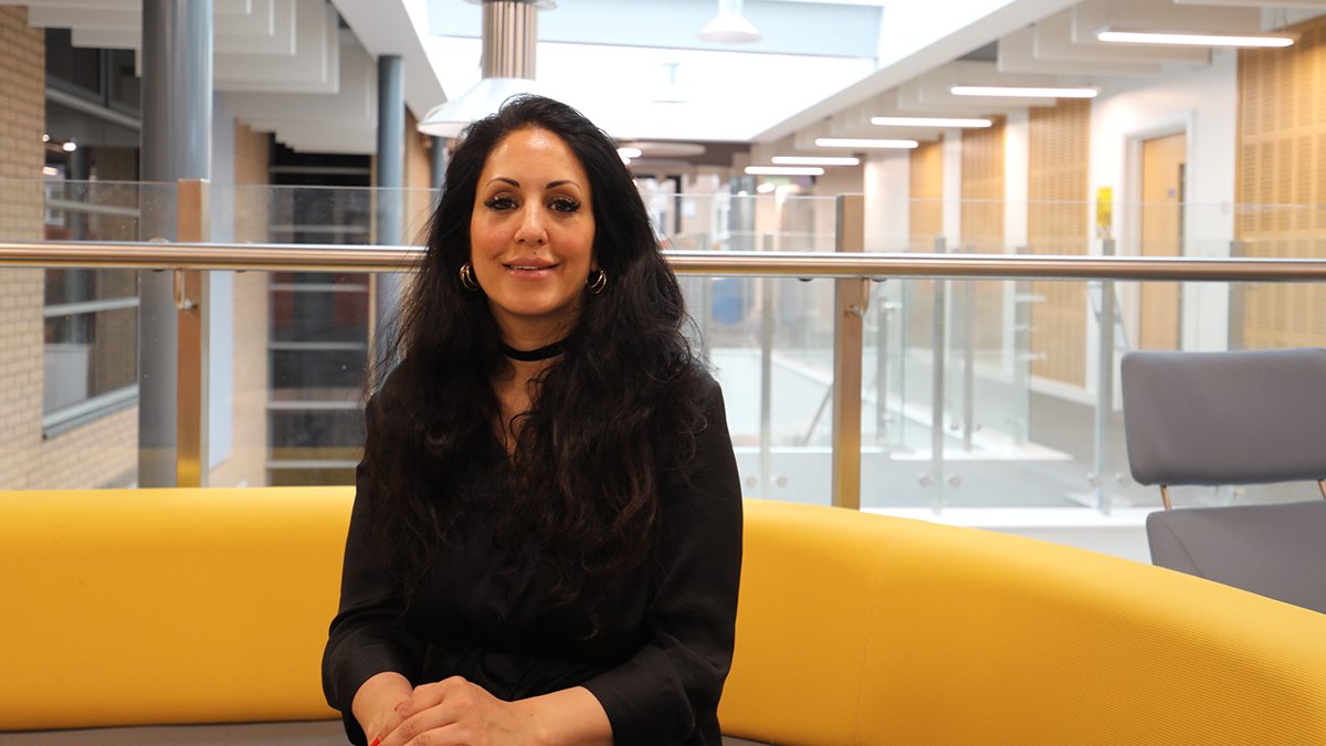 A woman with dark hair wearing a black outfit is smiling on a yellow sofa..