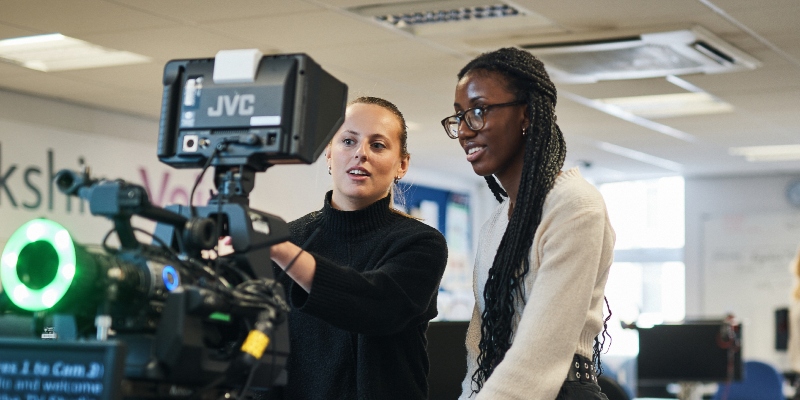 Two female journalism students setting up a camera and autocue.