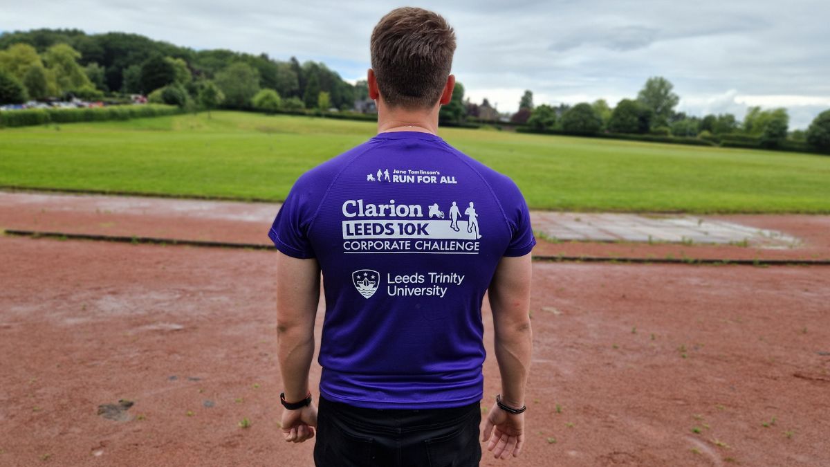 A man with dark hair wearing a purple tee shirt stands on a running track.