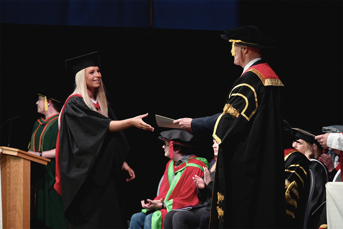 Student shaking hands with executive during graduation ceremony..