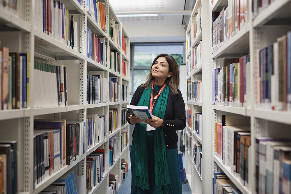 Student with book walks through the bookshelves in AKLC.